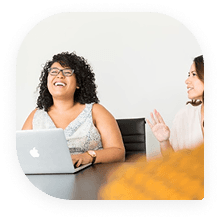 Mujeres riendo mientras trabajan juntas en un portátil